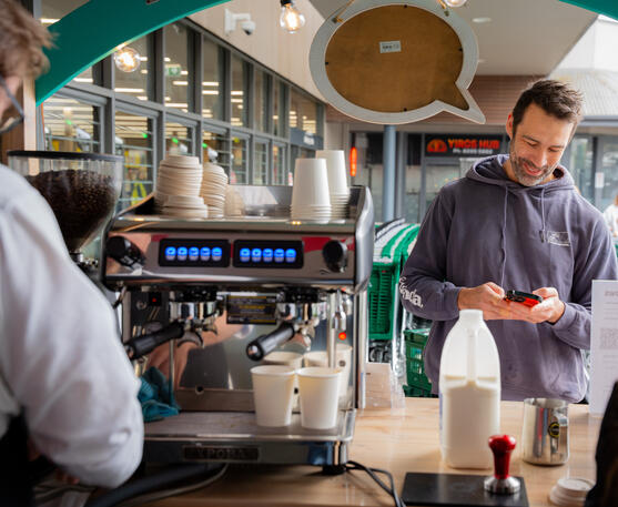 Connecting with our Adelaide customers over freshly roasted coffee. A male customer in a grey hoodie smiling at the barista behind an espresso machine.