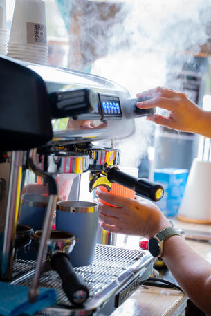 Attention to detail: pre-heating keep cups makes a difference to the taste of the coffee! Close-up of a barista's hands operating the steam wand on a commercial espresso machine.
