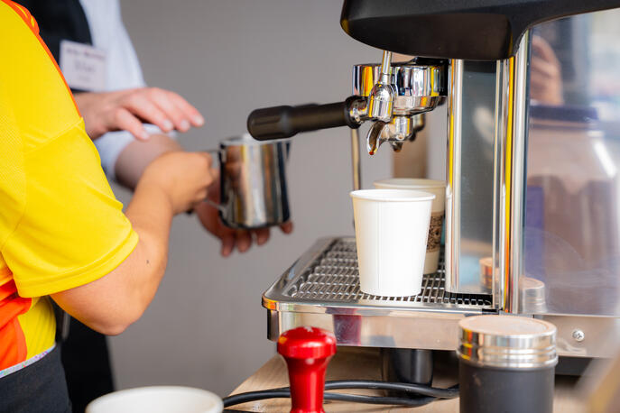 Espresso shots pouring from a commercial coffee machine portafilter into two paper cups.