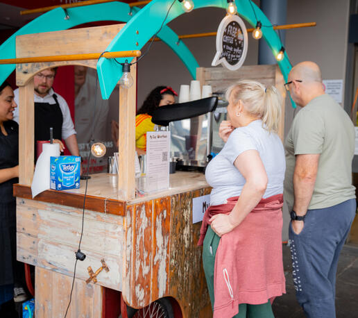 Customers standing at a rustic wooden coffee cart waiting for their beverage orders.