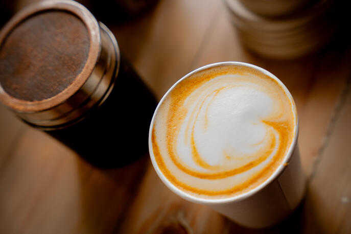 Beautiful coffee swirls made with passion and care. Top-down view of a latte with heart-shaped foam art next to a chocolate powder shaker.