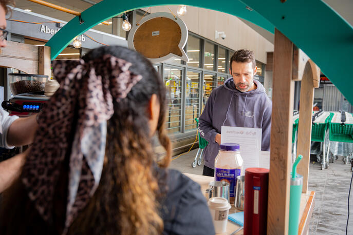 A woman interacting with a barista across the service counter of a wooden coffee cart.